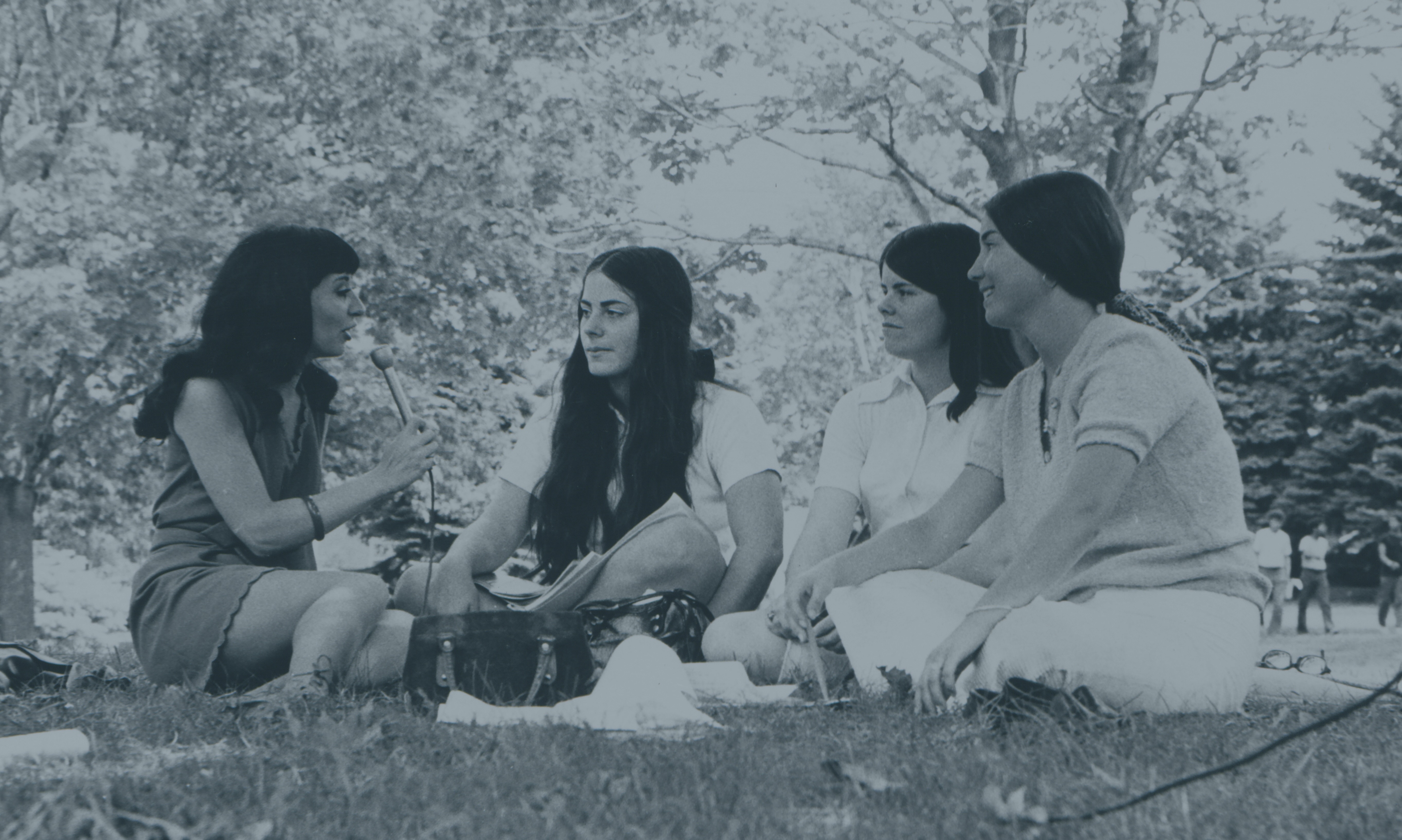 A group of Providence College students sitting on grass and speaking into a microphone.