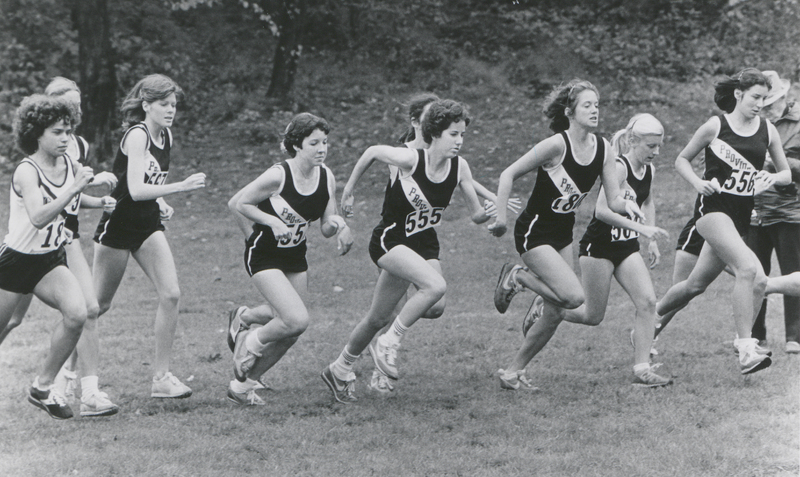 Several cross country runners wearing Providence College uniforms running along a field outside.