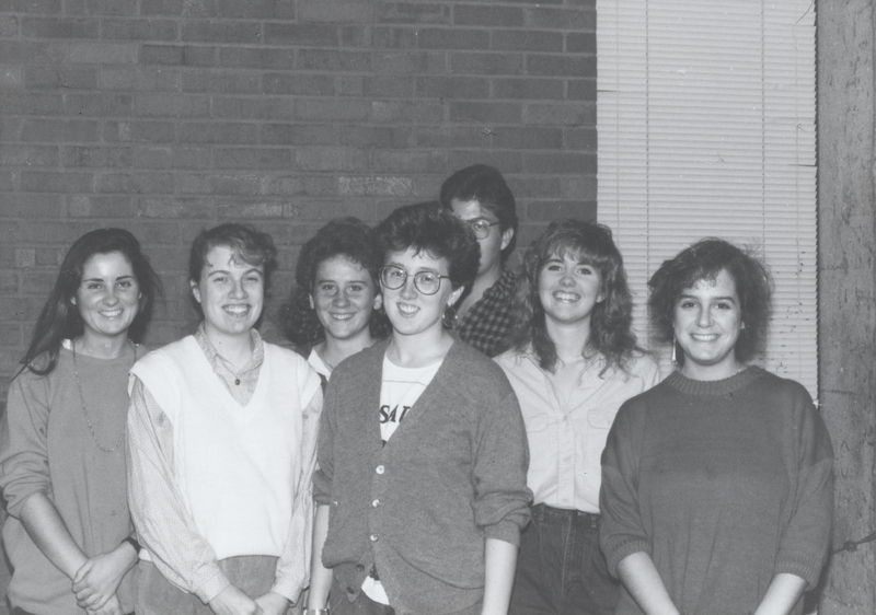 Several students pose for a photograph in brick walled room.