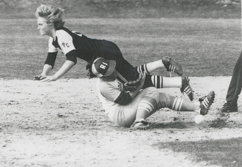 Softball game showing a player from Providence College sliding into a base while another player from the University of Rhode Island attempts to tag them out.
