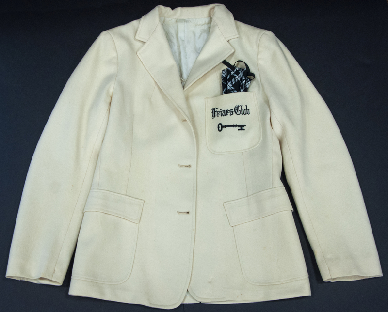 A Friars Club white jacket with a black and white checkered pocket square. The words 'Friars Club' and a key are embroidered on the front pocket.