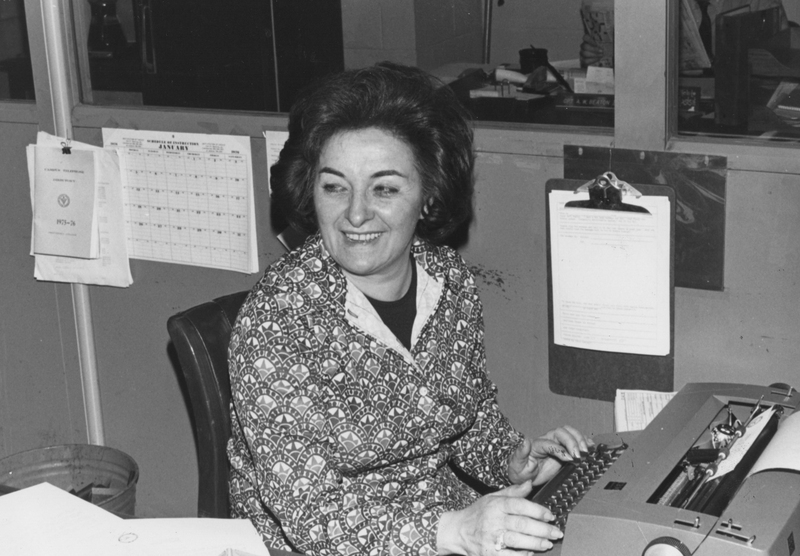 Olga D'Arezzo sits at a desk in an office with a typewriter.
