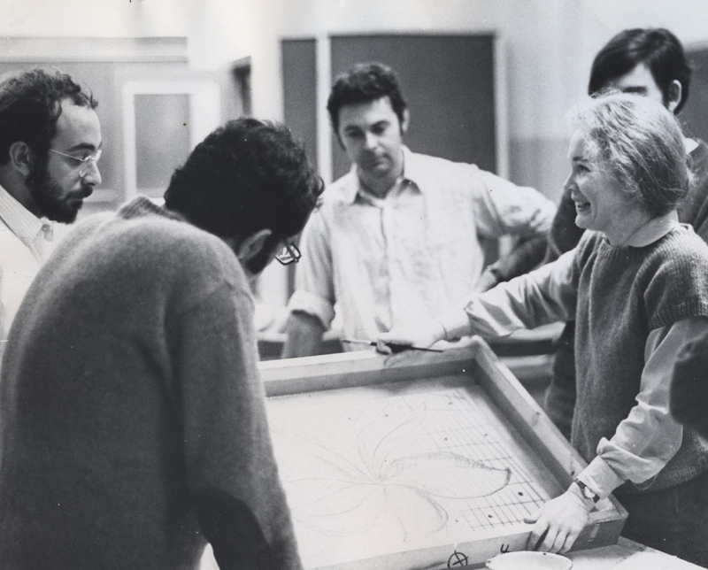 Suzanne D'Avanzo standing with students in a classroom holding a canvas.