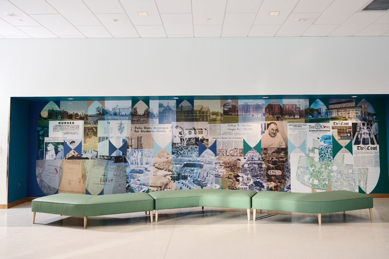 Modern lobby with a long green modular bench in front of a mural made of historical photos and newspaper clippings arranged in a geometric collage.