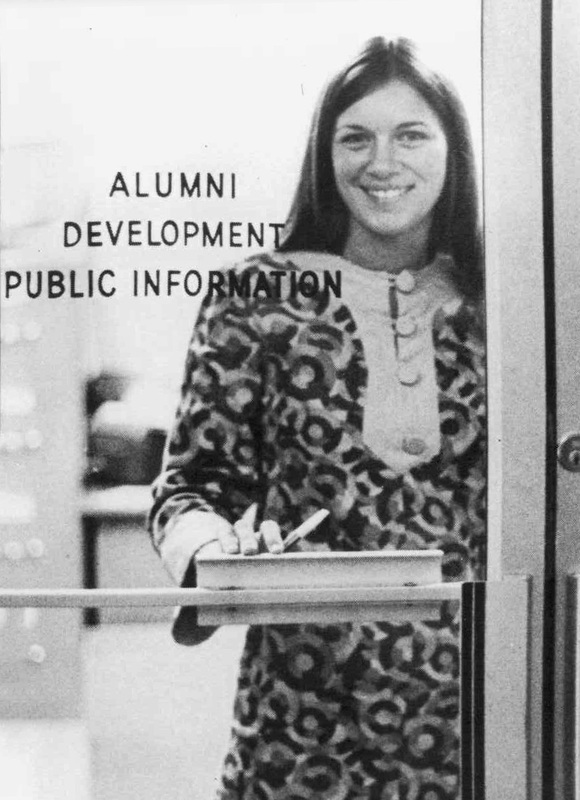 Karen Roy standing in front of a glass door that reads 'Alumni Development Public Information.'