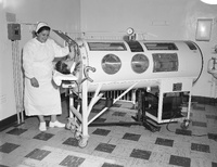 A nurse attending to a patient inside an iron lung machine, with medical equipment in the background.