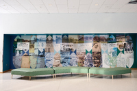 Modern lobby with a long green modular bench in front of a mural made of historical photos and newspaper clippings arranged in a geometric collage.