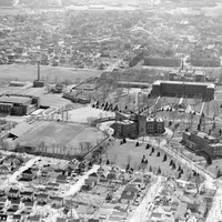 Aerial view of Providence College with multiple buildings, open fields, tree-lined paths, and a surrounding residential neighborhood.