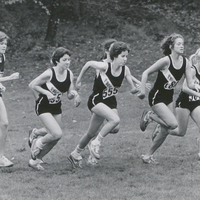 Several cross country runners wearing Providence College uniforms running along a field outside.