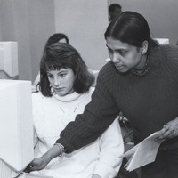 Nazma Latif-Zaman stands next to a student helping them with a computer.