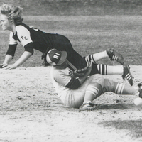 Softball game showing a player from Providence College sliding into a base while another player from the University of Rhode Island attempts to tag them out.