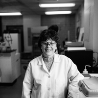 Kathleen Cornely poses for a photograph in a laboratory wearing a lab coat and safety glasses.