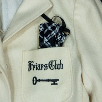 Close up of the Friars Club embroidered logo on a white blazer. The logo is of a key.