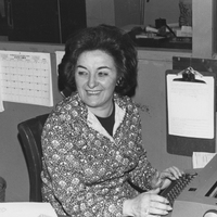Olga D'Arezzo sits at a desk in an office with a typewriter.