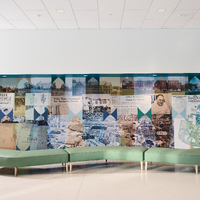 Modern lobby with a long green modular bench in front of a mural made of historical photos and newspaper clippings arranged in a geometric collage.